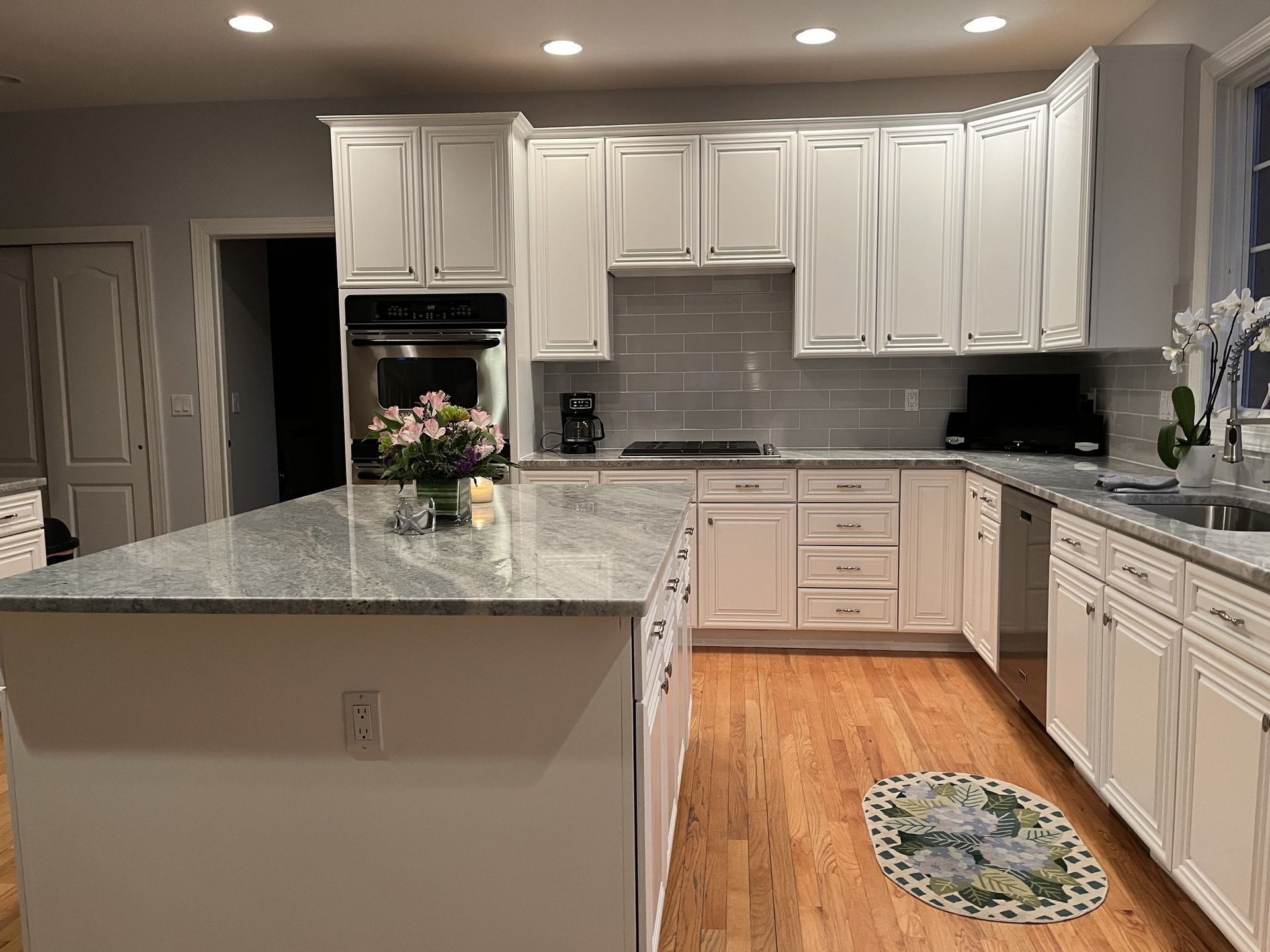 White kitchen with granite countertops, wooden floors, and a center island, featuring modern white cabinetry and appliances.