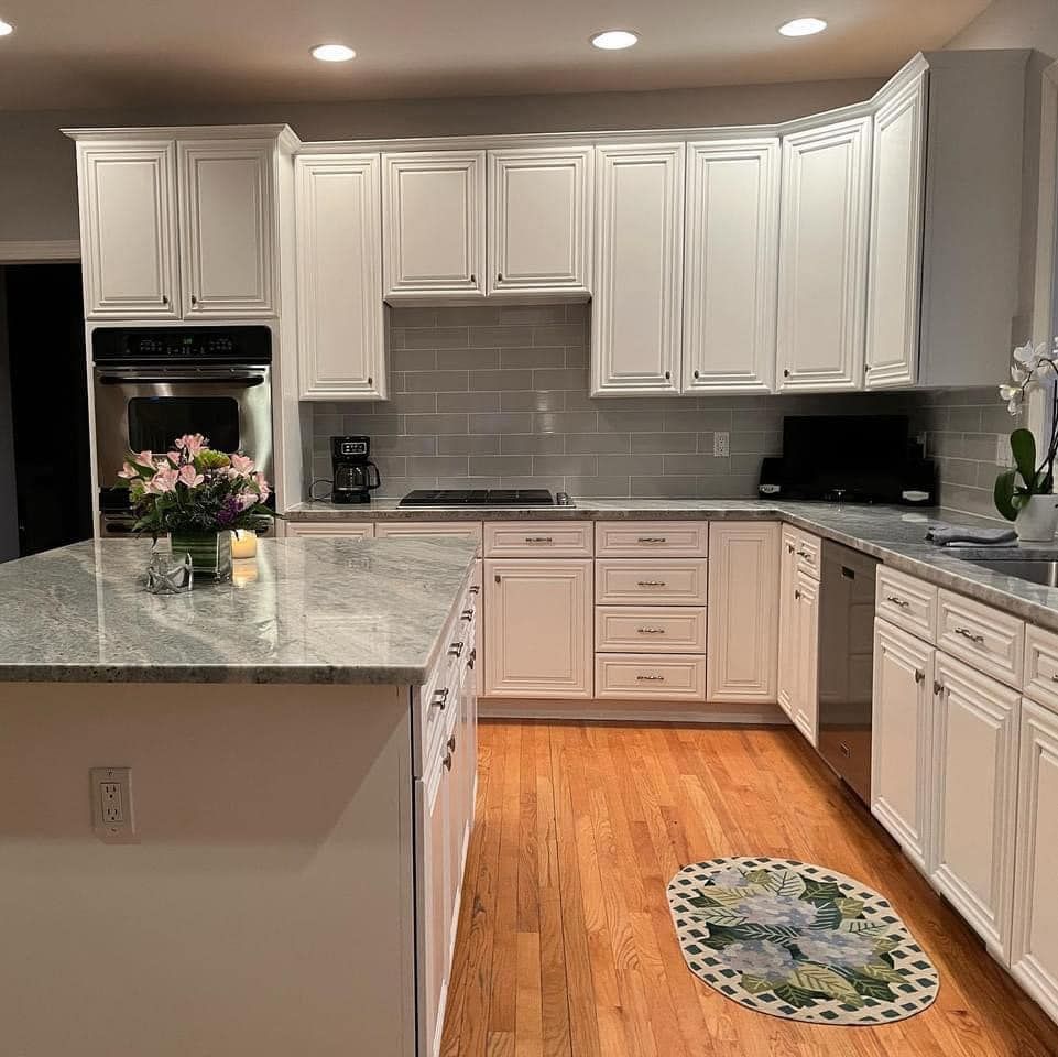 A bright kitchen with white cabinets, light gray granite countertops, stainless steel oven, and light wood flooring.