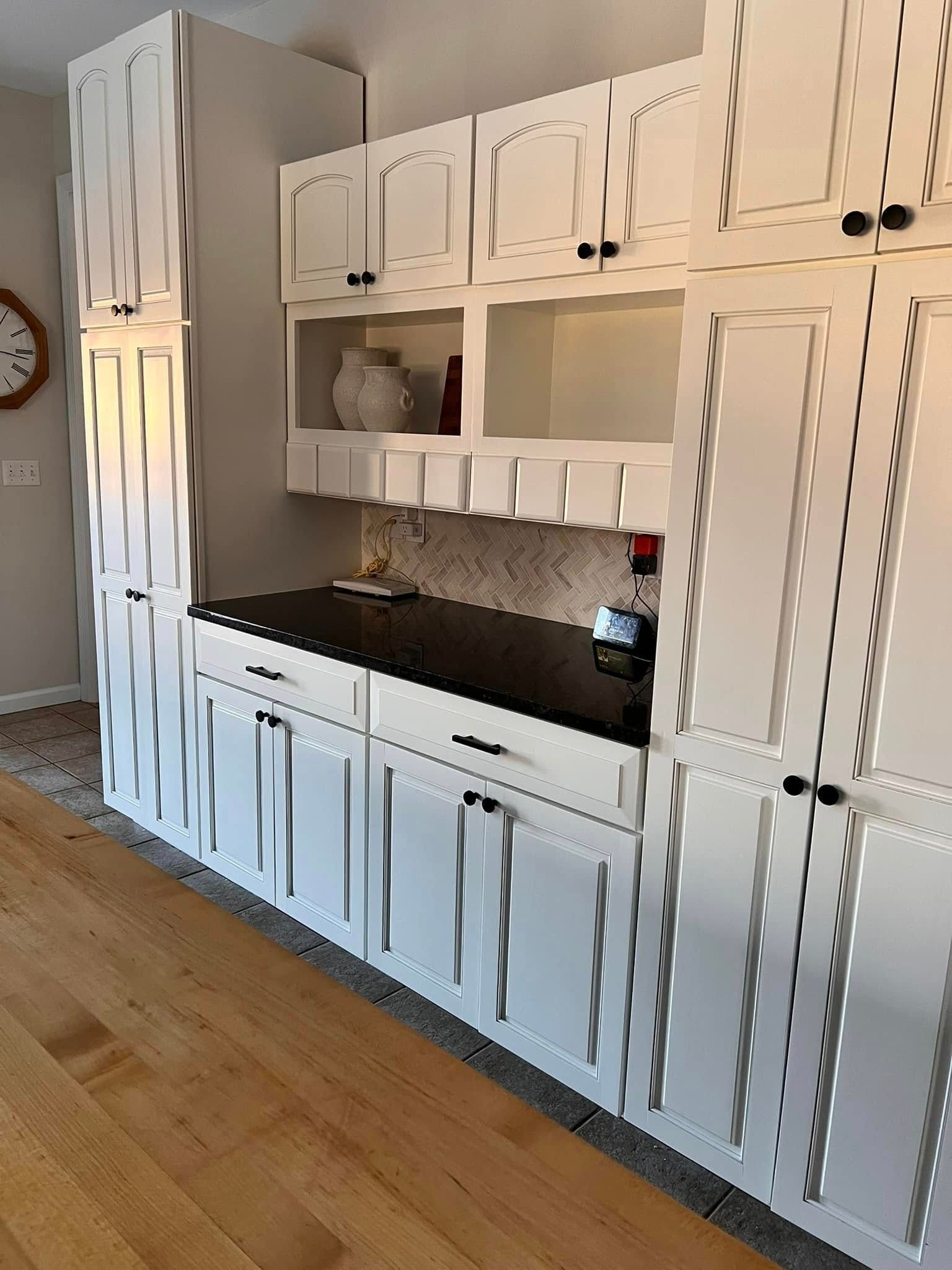 White kitchen cabinets and drawers with dark countertops, situated along a wall in a room with light wood floors.