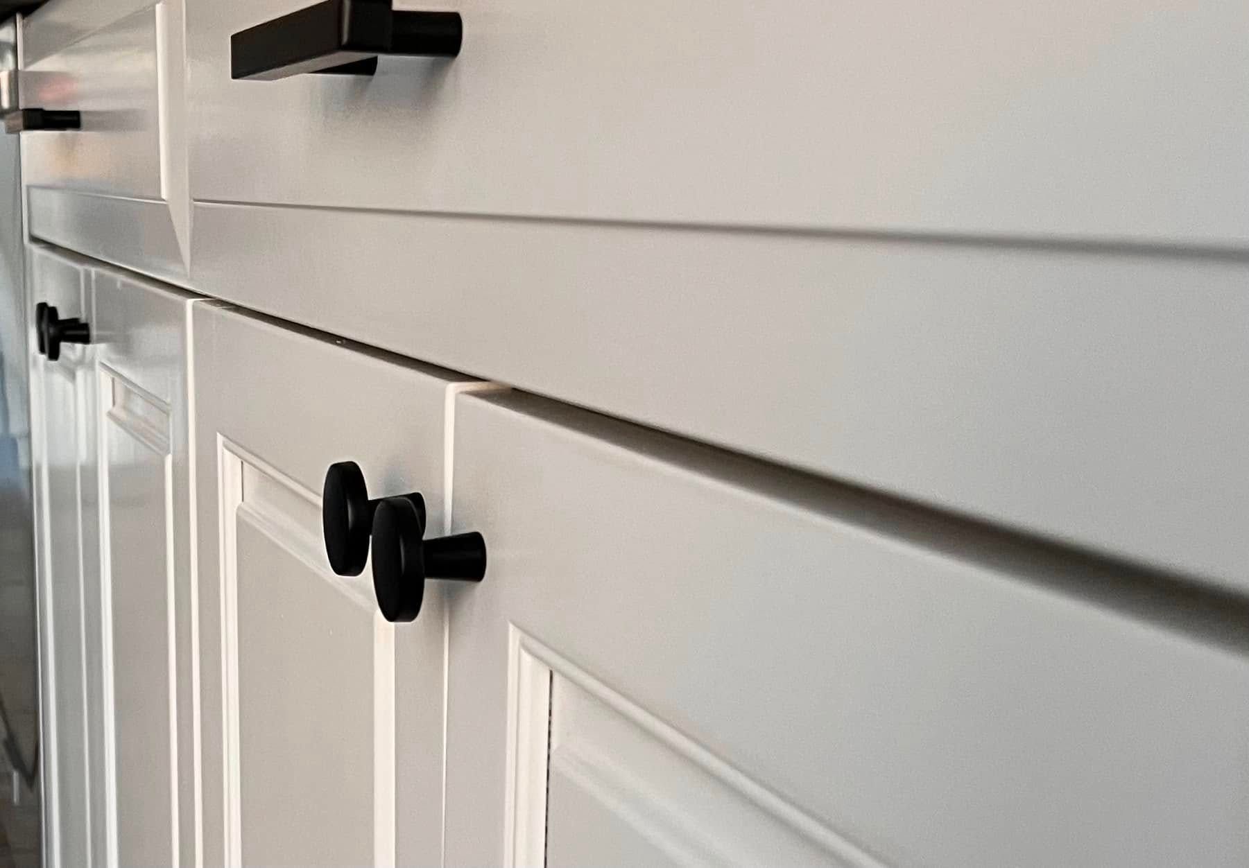 Close-up of white kitchen cabinets with black drawer pulls and knobs.