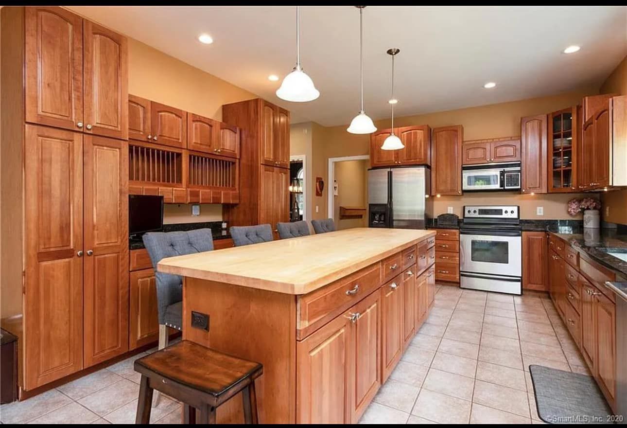 A spacious kitchen with light wood cabinets, an island with a wooden countertop, and stainless steel appliances.