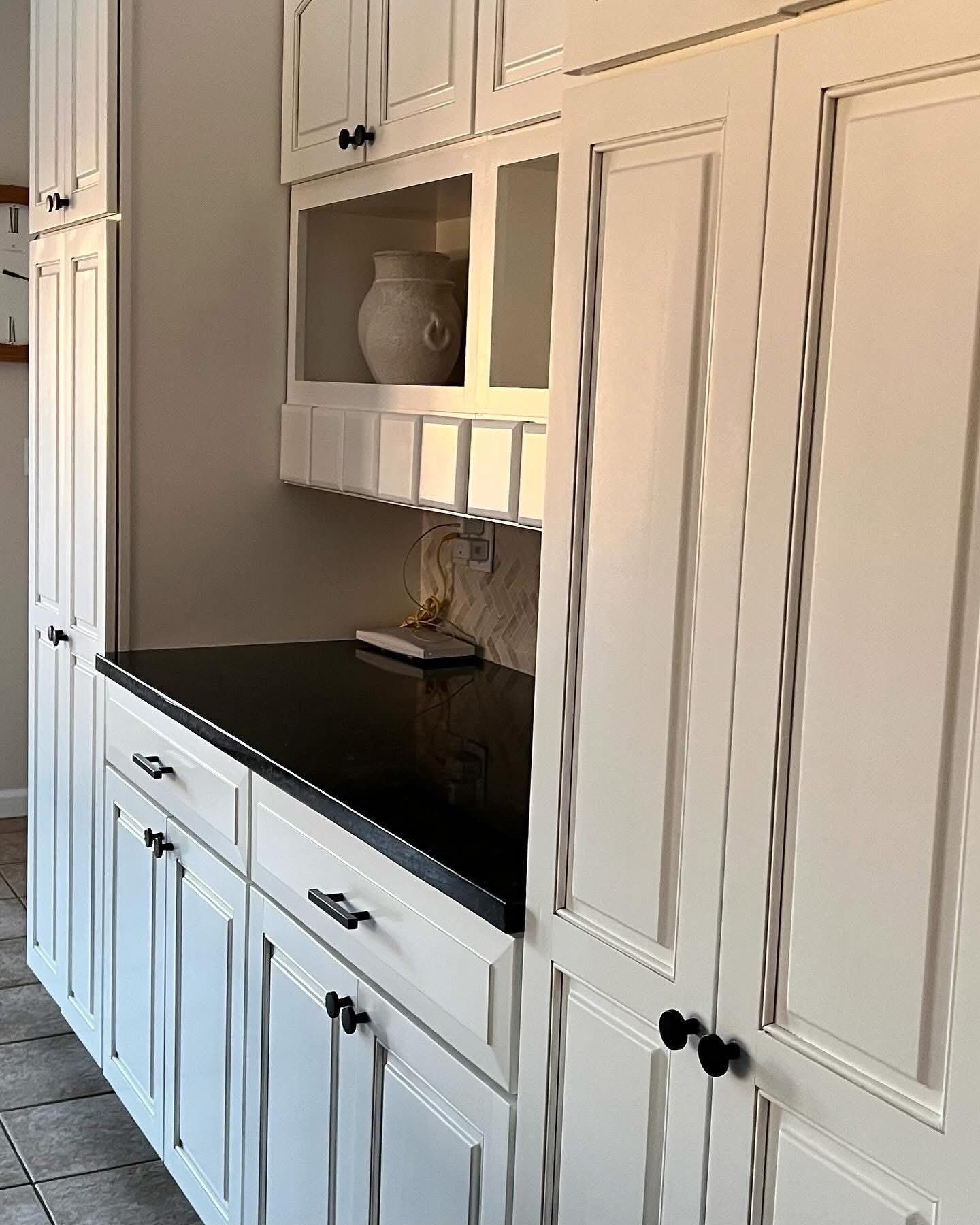 White cabinetry with black hardware and a dark countertop in a kitchen setting.