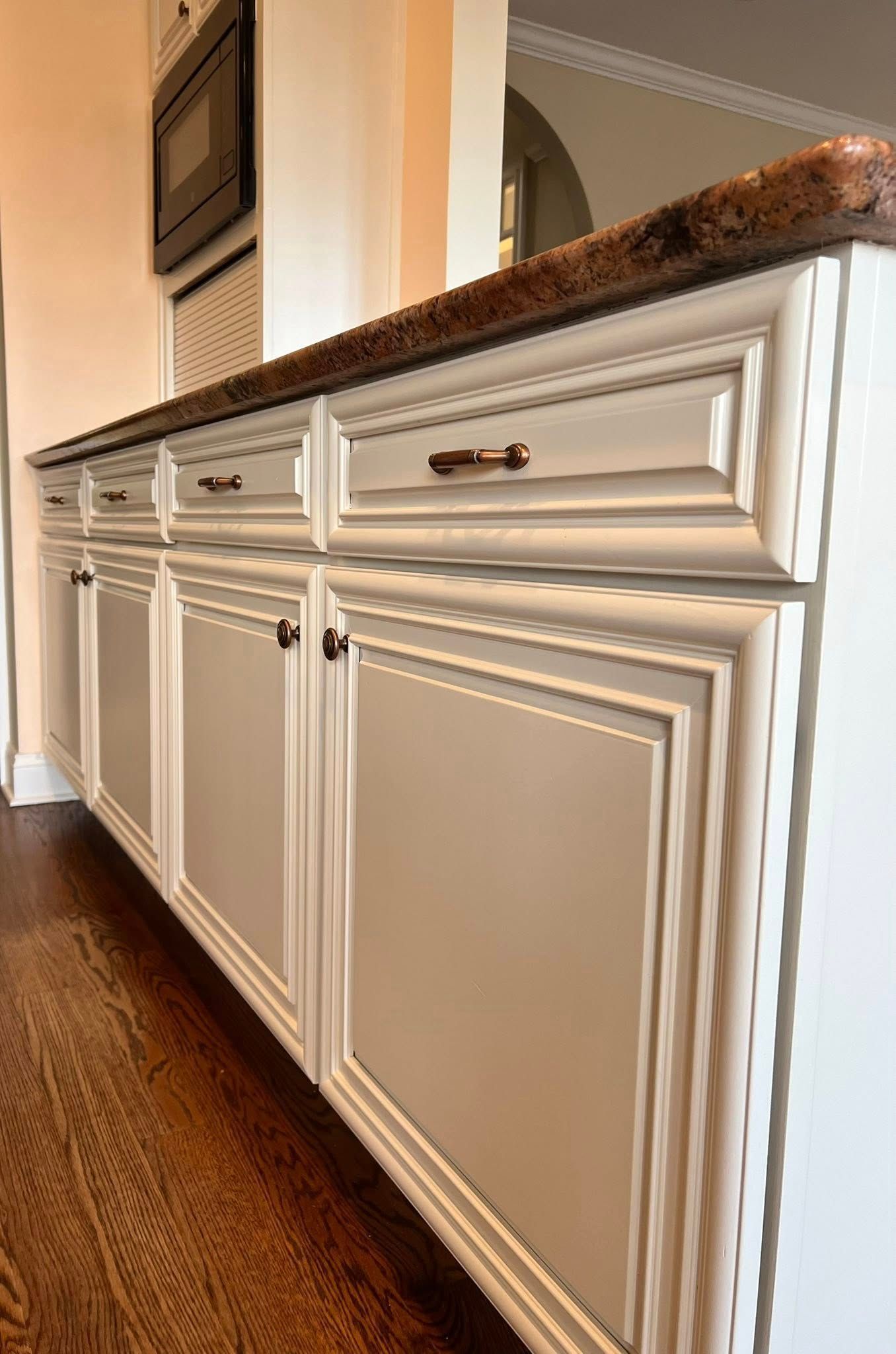 Off-white kitchen cabinets with decorative molding and bronze hardware, set against a dark hardwood floor.