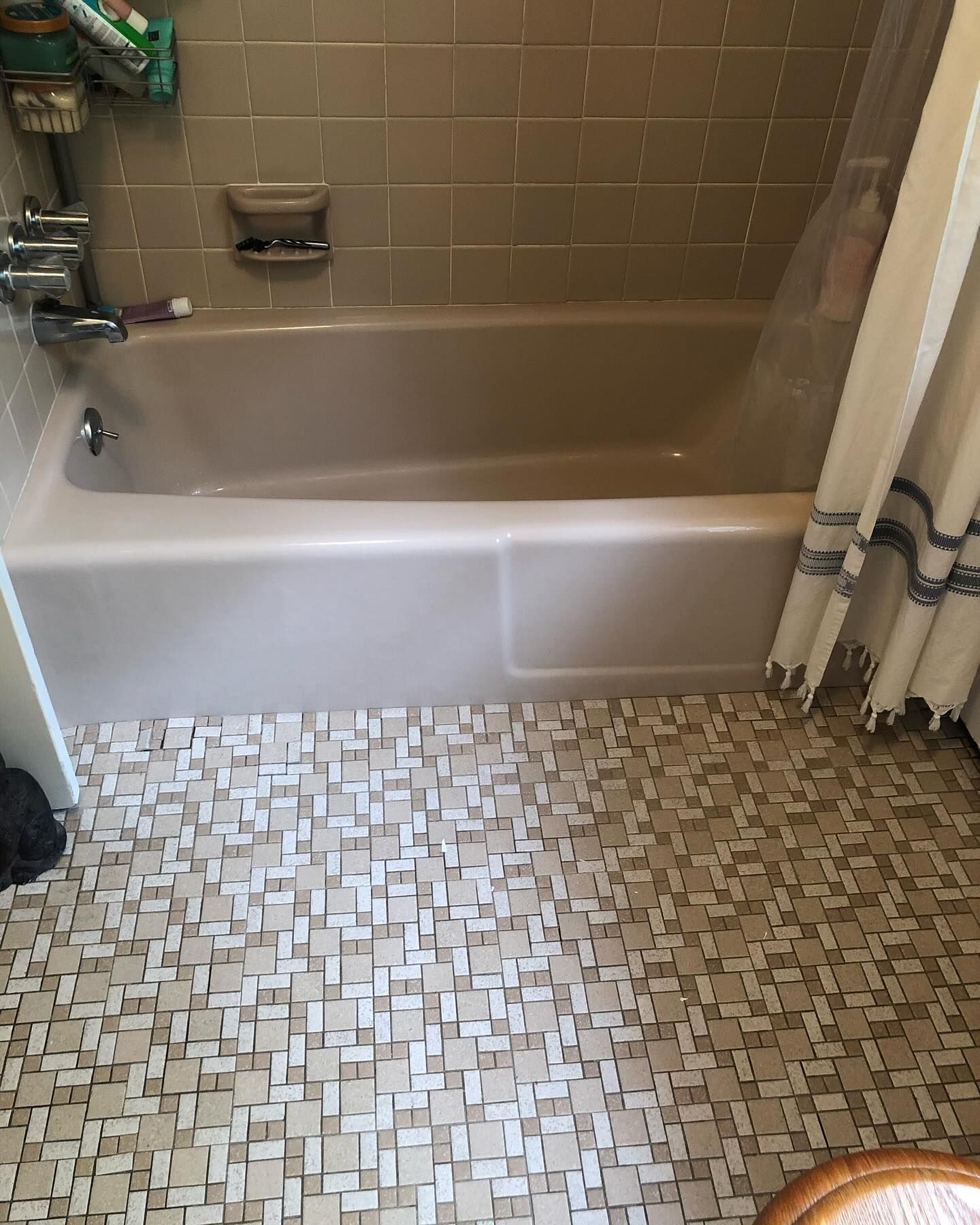 A beige bathtub with a matching tile surround and mosaic-patterned flooring in a bathroom.