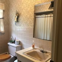 A small bathroom with floral wallpaper, white wall tiles, a vanity sink, a toilet, and a mirror with a shower curtain.