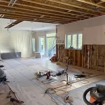 A home interior during renovation, featuring exposed wooden ceiling joists, unfinished walls, and covered flooring.
