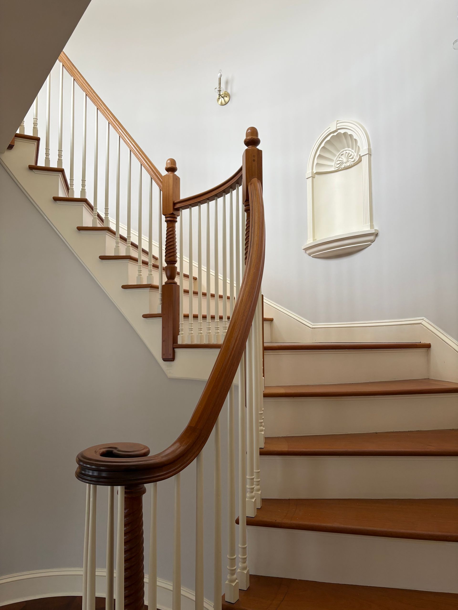 A curved wooden staircase with white balusters and risers, featuring a decorative wall niche on the landing.