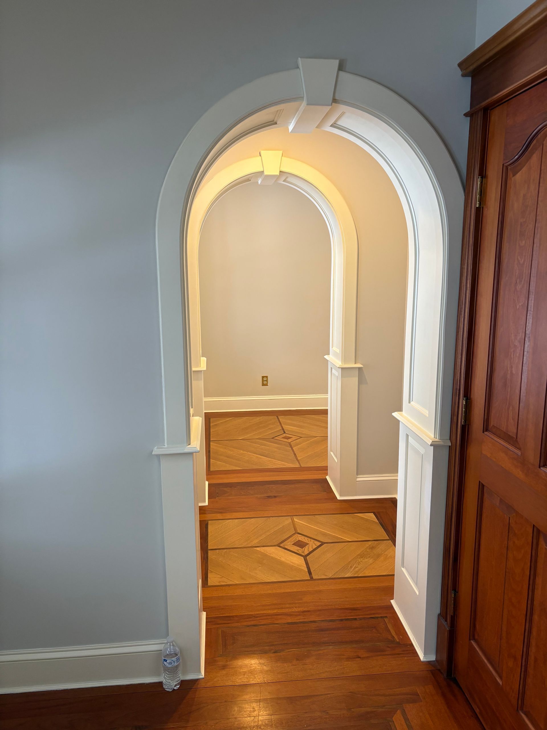 An arched doorway with decorative white trim leads into a hallway with hardwood floors and a second matching archway.