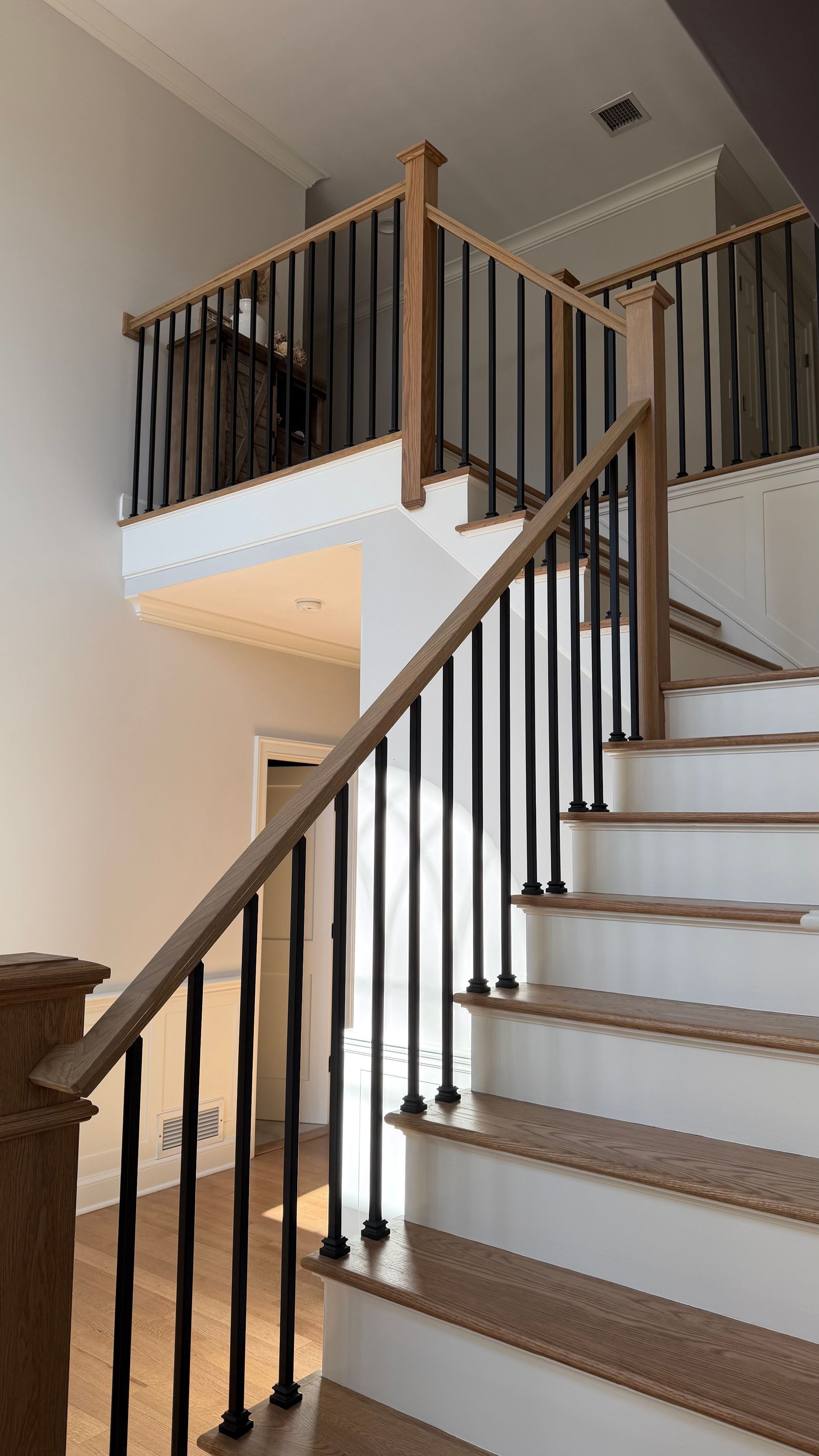 A wooden staircase with white risers, wood treads, and a black baluster railing in a modern home.