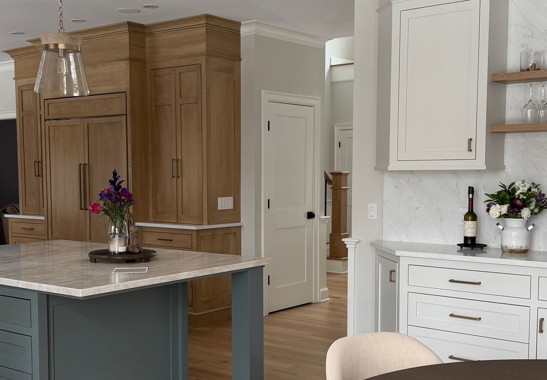 Modern kitchen featuring a blue island, wood-paneled refrigerator wall, white cabinets, and marble countertops.