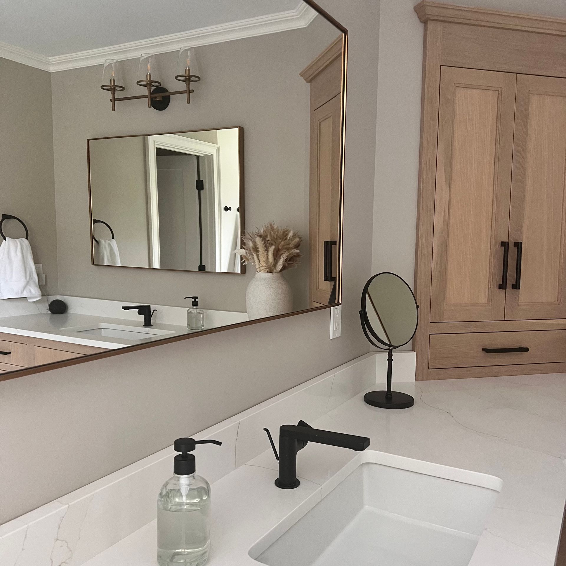 Bathroom with white countertop, black faucet, and large mirror reflecting the room, including a wooden cabinet.