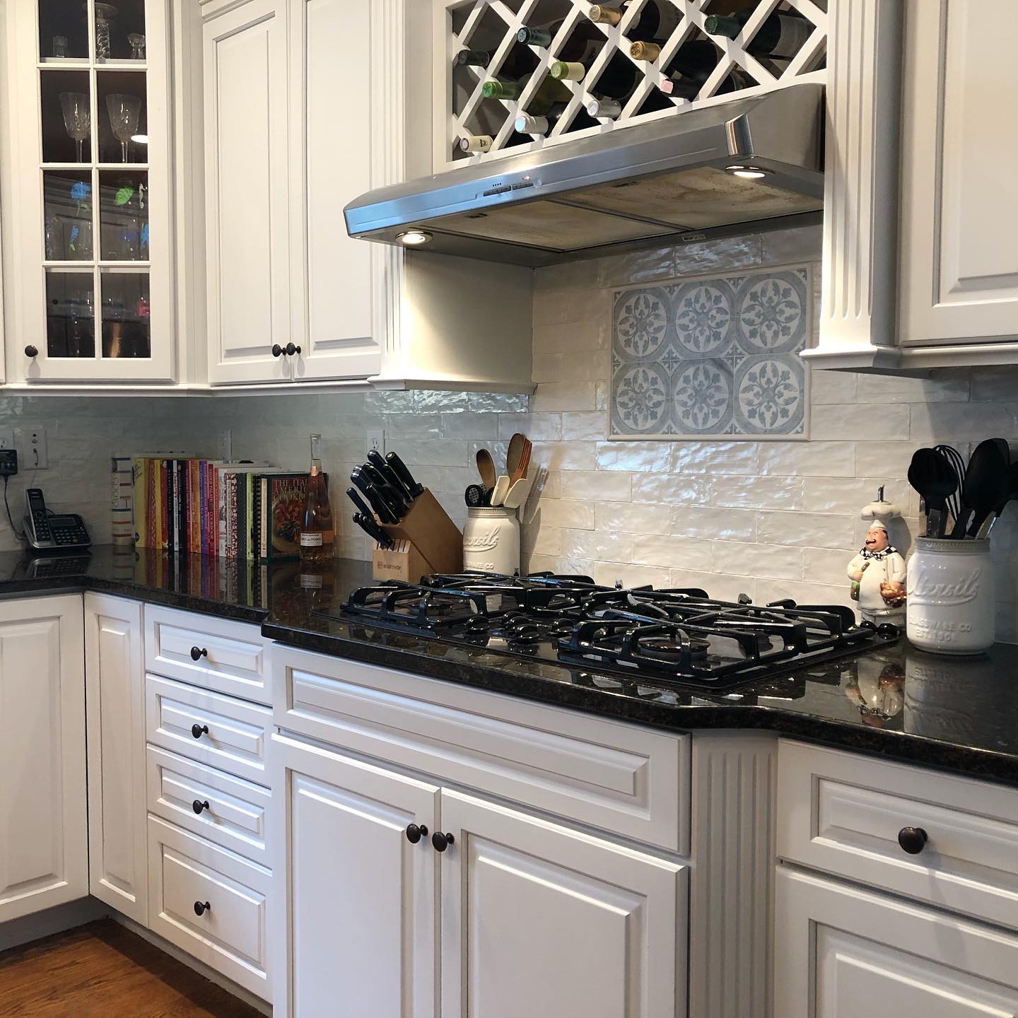 White kitchen with black countertops, a gas stovetop, and a wine rack above it.
