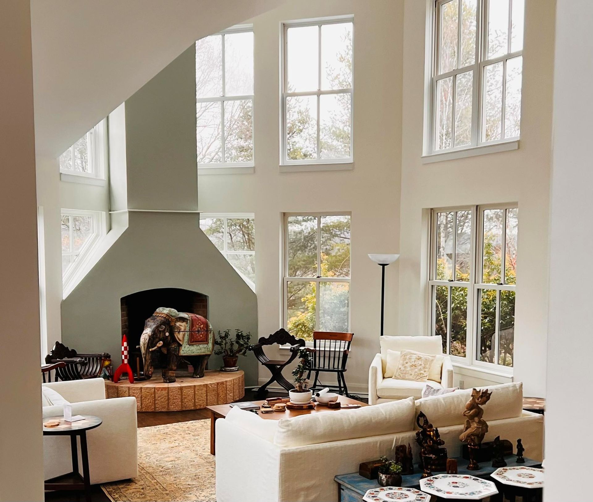 Living room with fireplace, high ceilings, large windows. White sofa, chairs, rug.