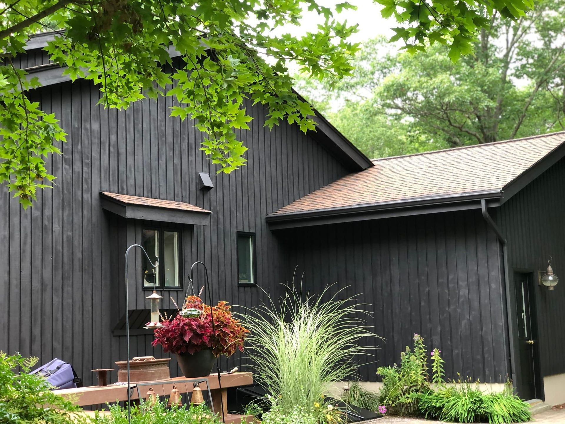 A black house with a brown roof is surrounded by trees.