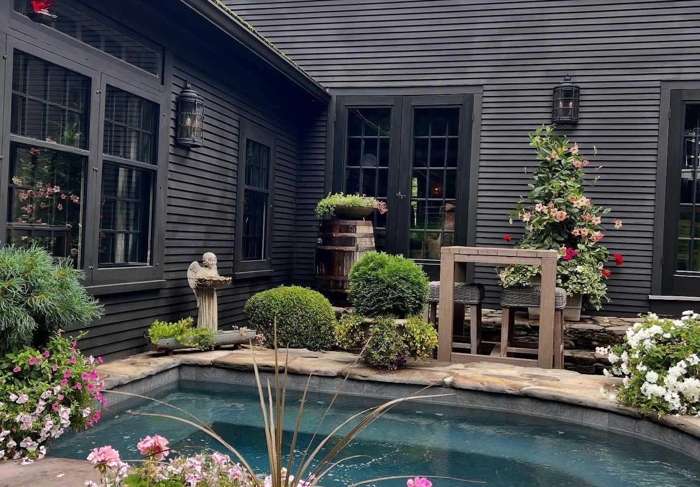 Black building facade with a stone patio, pool, and potted plants.