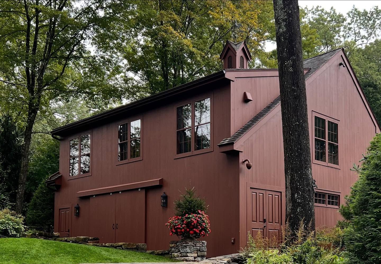 Brown two-story house with multiple windows and a small flower arrangement in front, surrounded by trees.