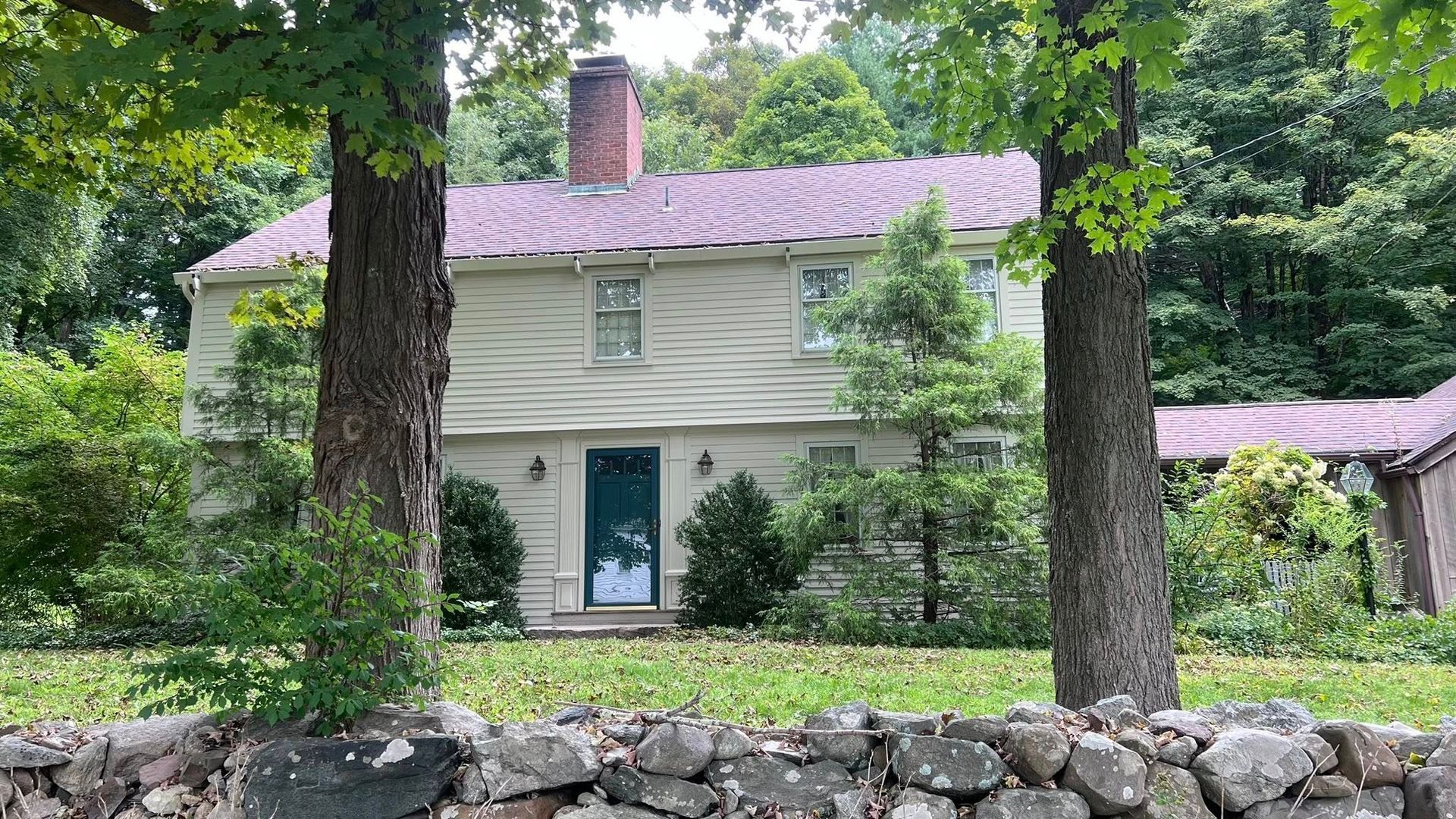 Beige two-story house with a red roof, a dark green door, and a stone wall in front.
