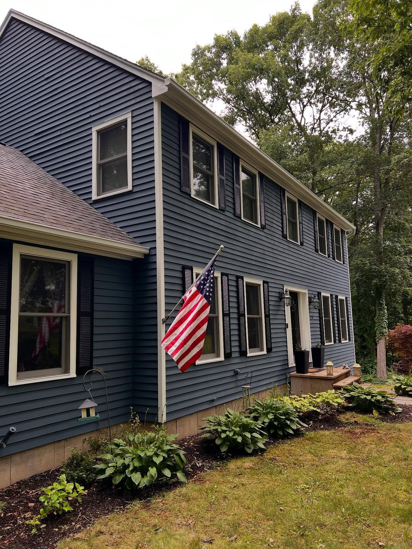 Two-story house with blue siding, white trim, black shutters, and an American flag.