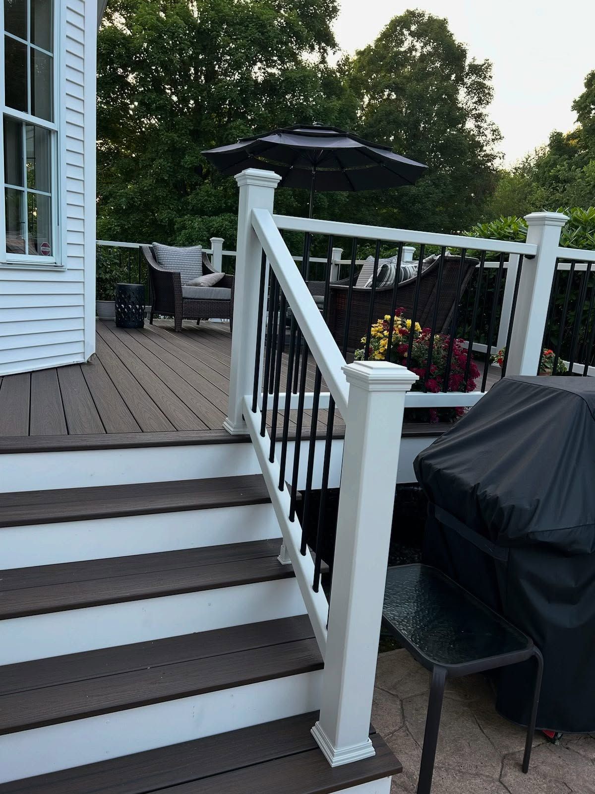 Wooden deck with stairs, white railing with black spindles, and outdoor furniture.