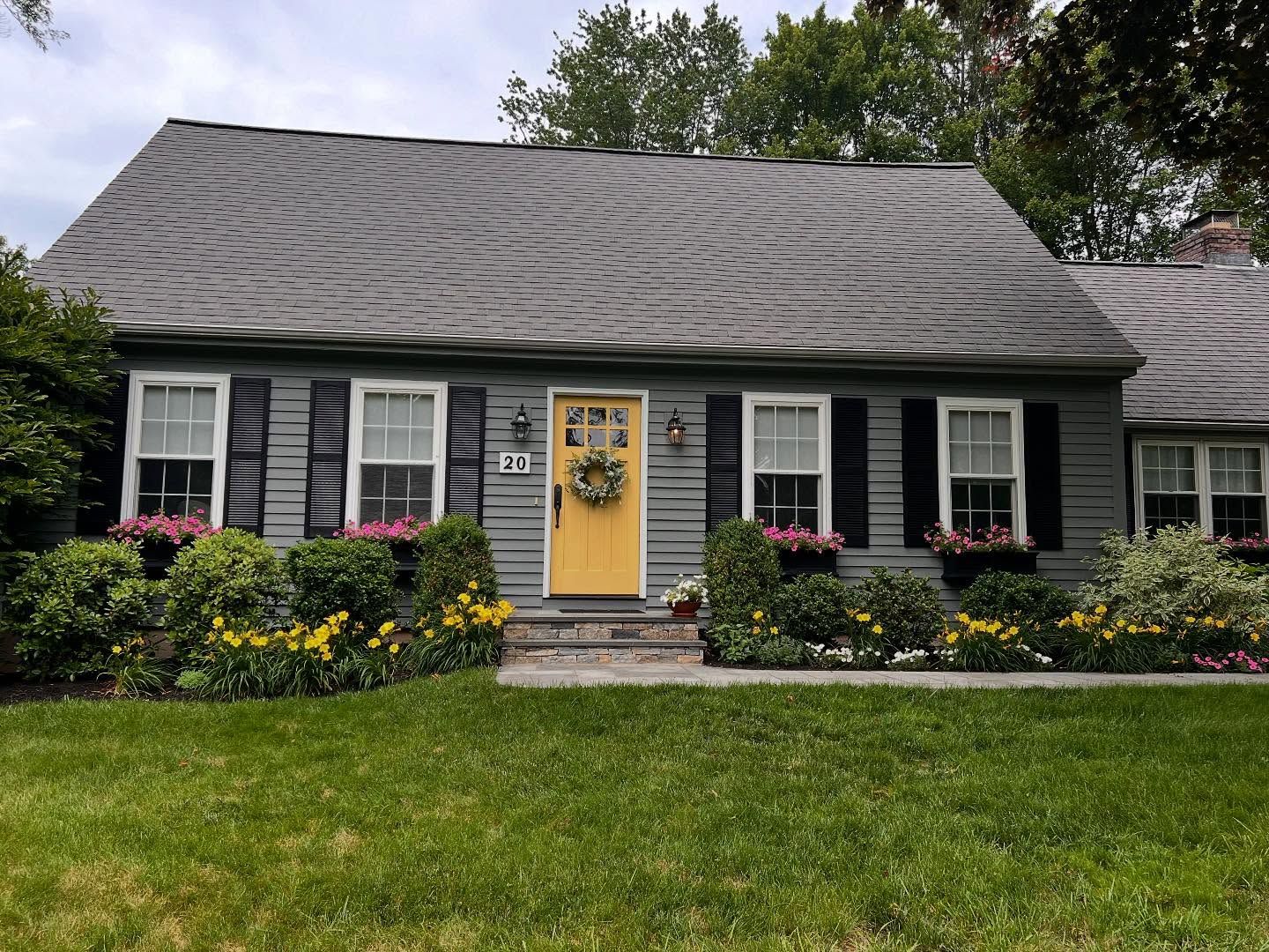 Gray house with yellow door, black shutters, and flower boxes; green lawn.