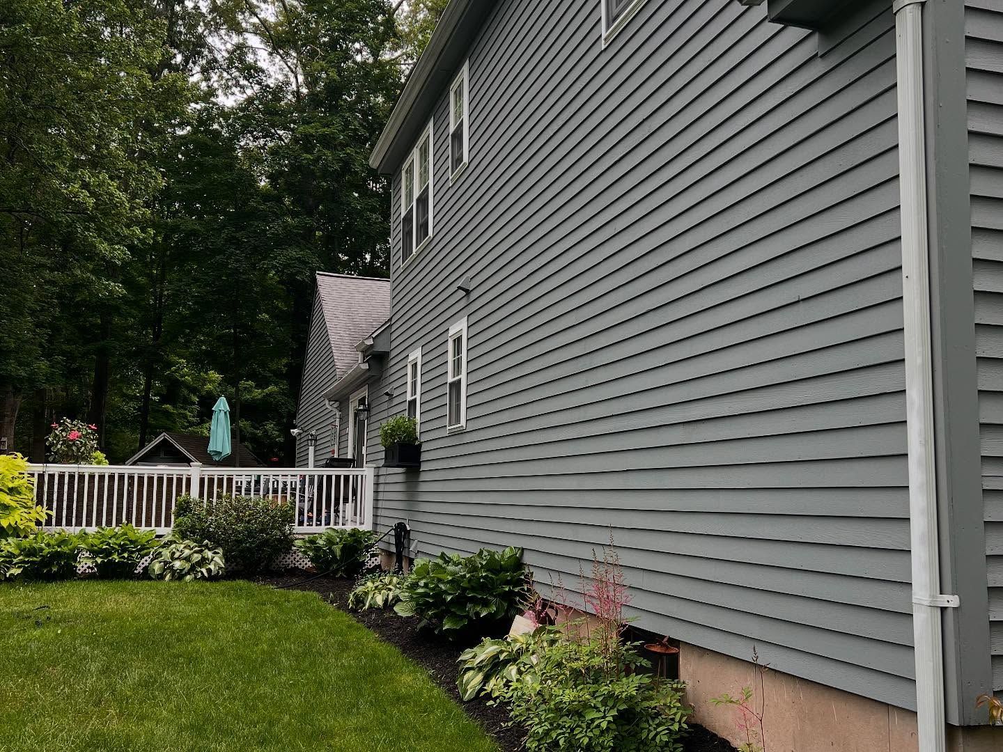 Gray house with siding, white deck, green lawn, and lush landscaping.
