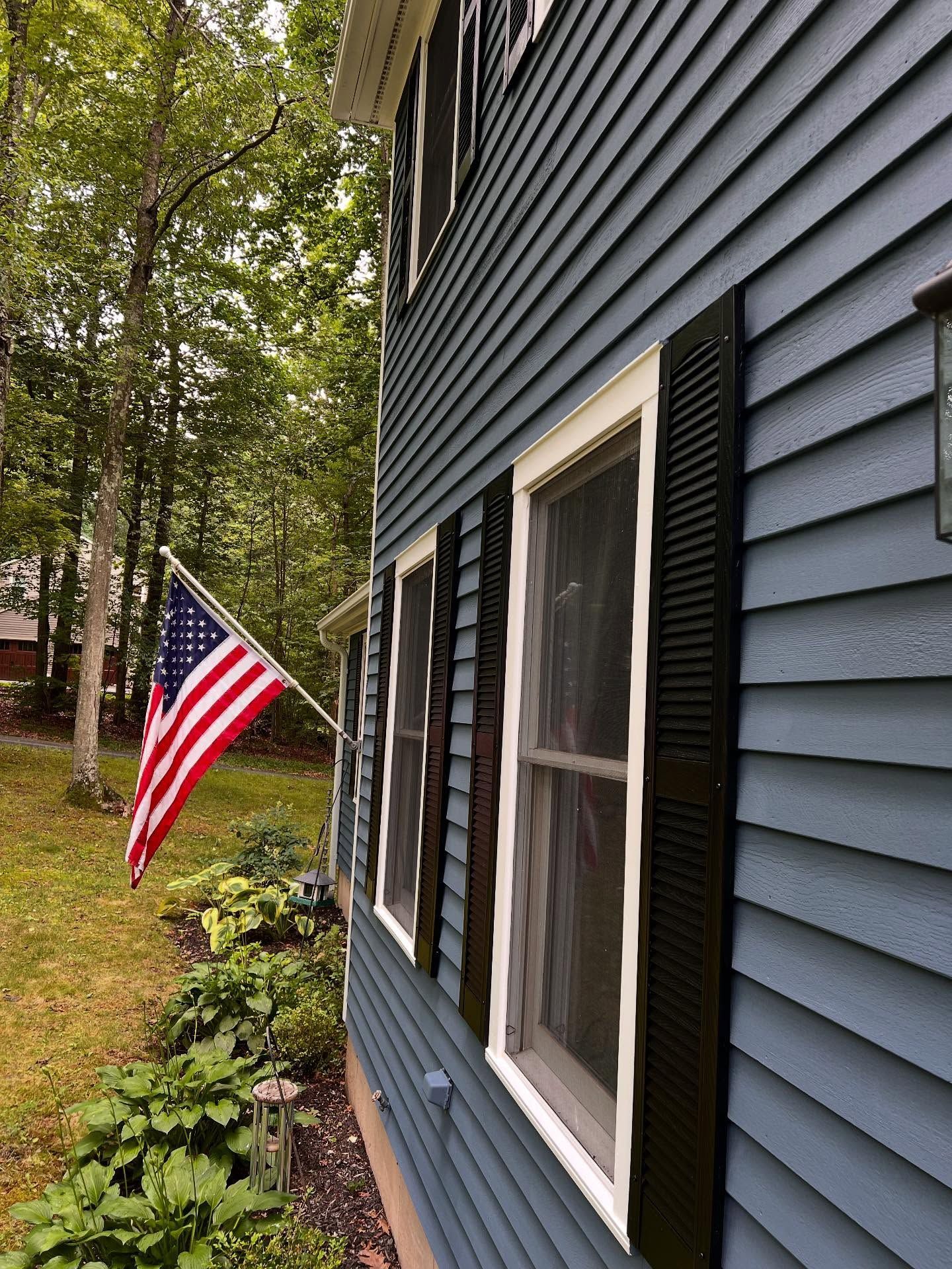 Side of a blue house with white trim, black shutters, and an American flag.