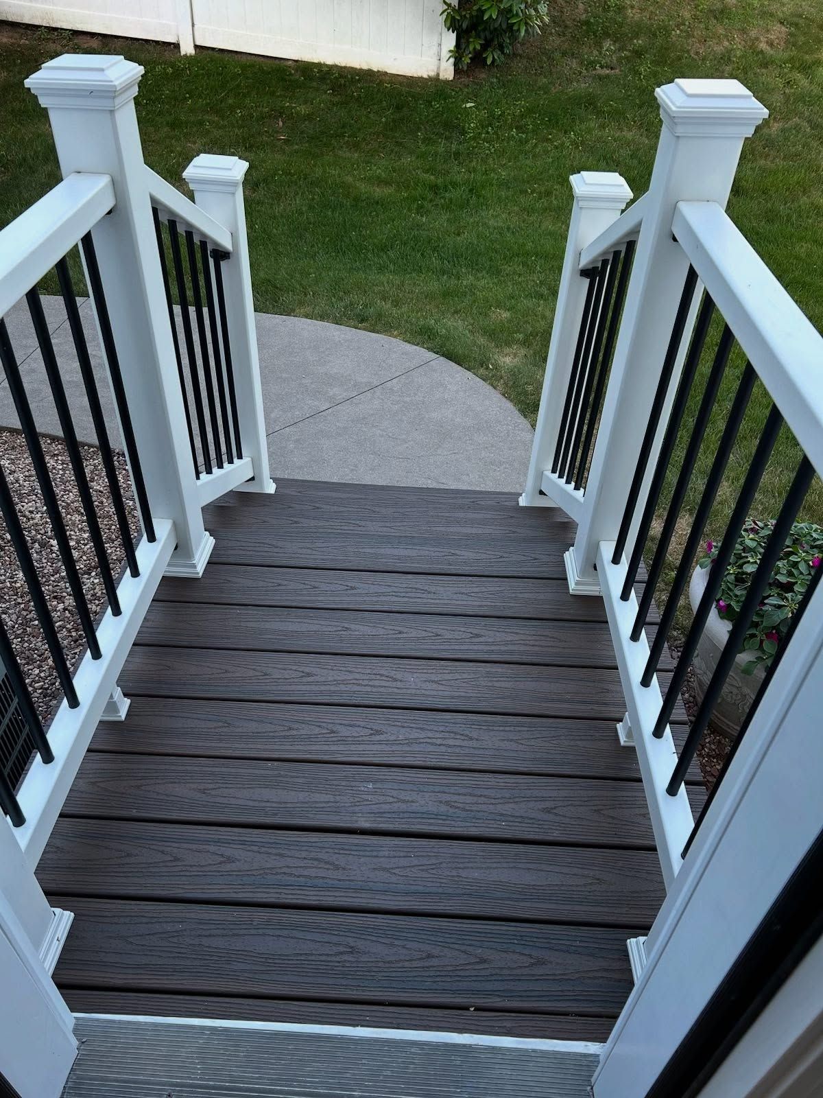 Wooden deck with white railings, black vertical bars, leading to a curved concrete walkway, grassy yard.