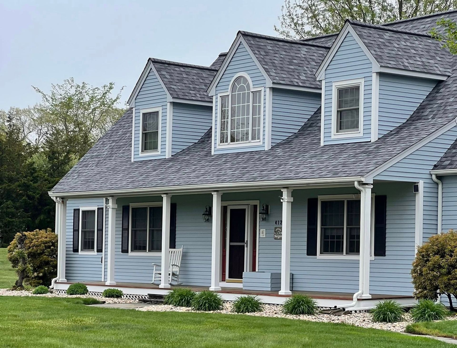 Blue house with dark gray roof, white trim, and a porch. Green lawn in front.