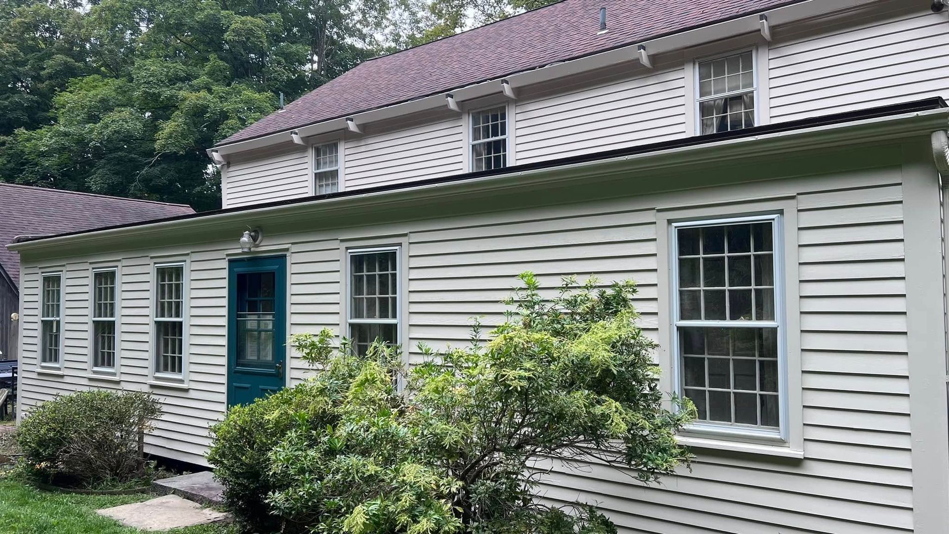 White clapboard house with green trim and door, multiple windows. Purple roof.