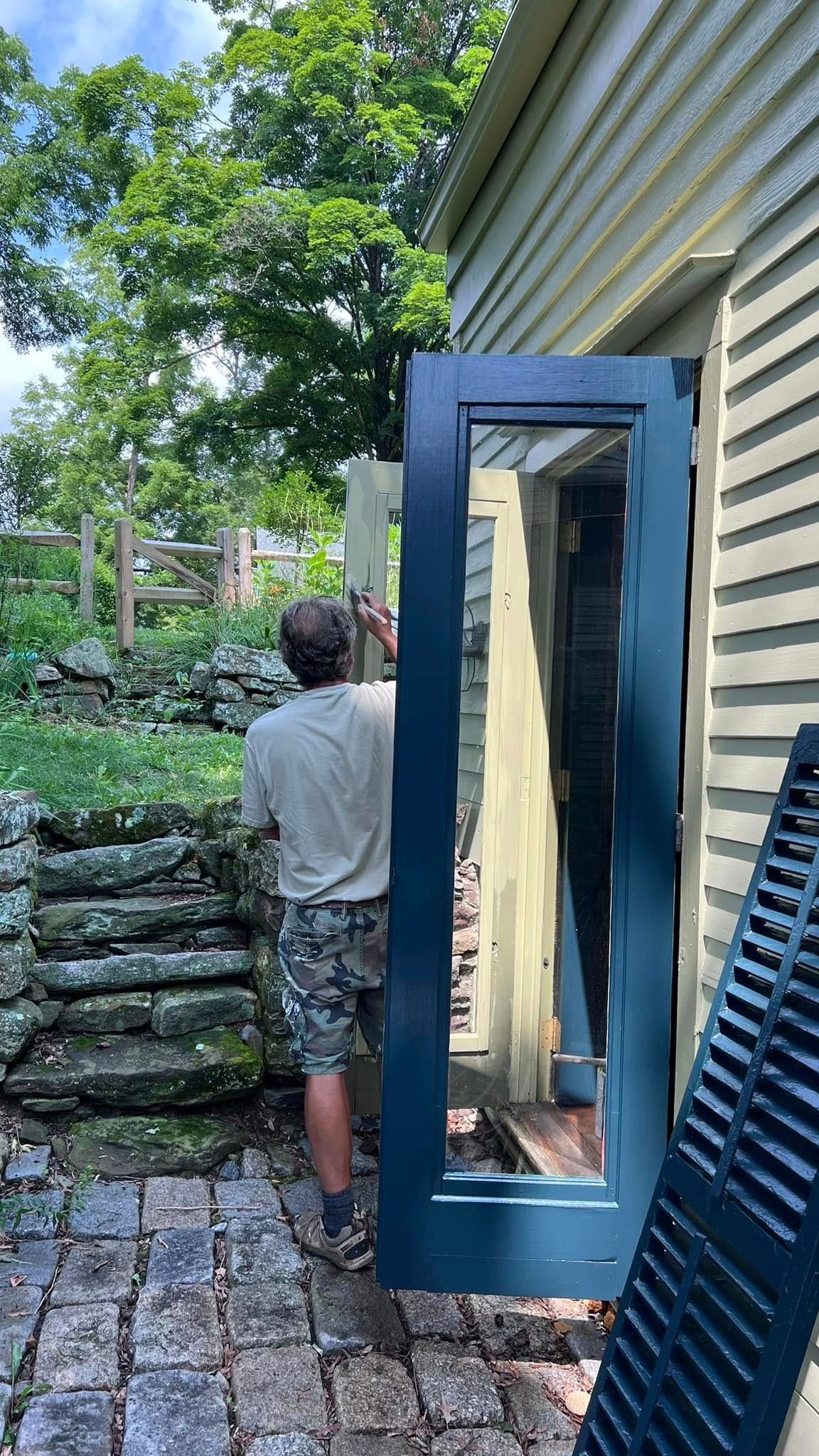 Person installing a dark blue door on a yellow house exterior, on a stone patio.