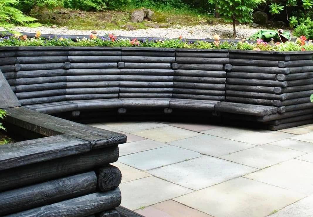 Curved dark wood bench surrounding a garden bed on a stone patio.