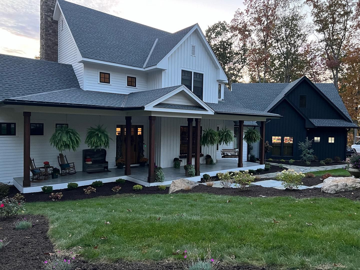White farmhouse with dark trim and a black side addition, on a grassy lawn.