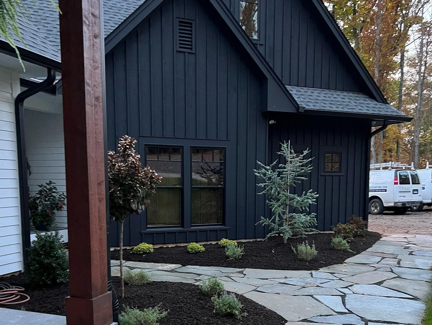 Black-painted house with dark roof and landscaping, stone pathway, and a brown post on the left.