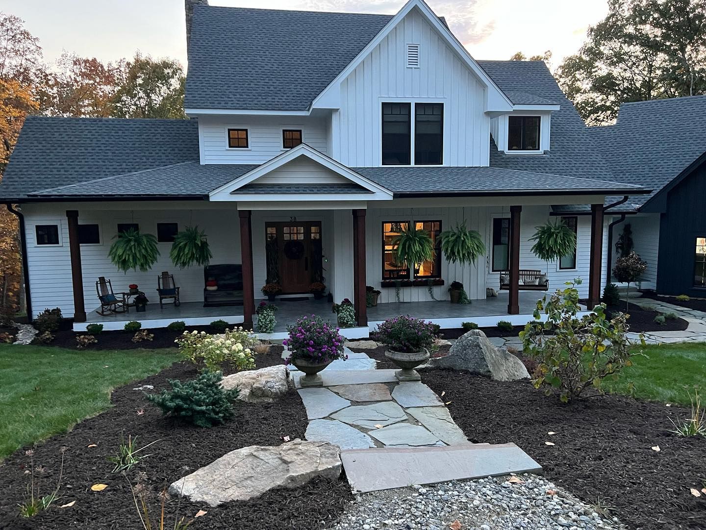 White farmhouse with a gray roof, front porch, and stone pathway leading to the door.