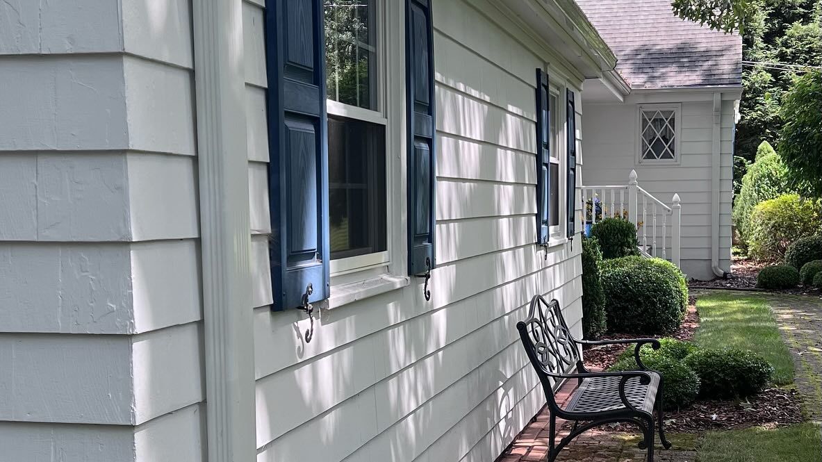 White house exterior with blue shutters, a bench, and a garden pathway.