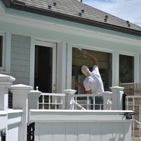 A man is painting a window on a porch of a house.