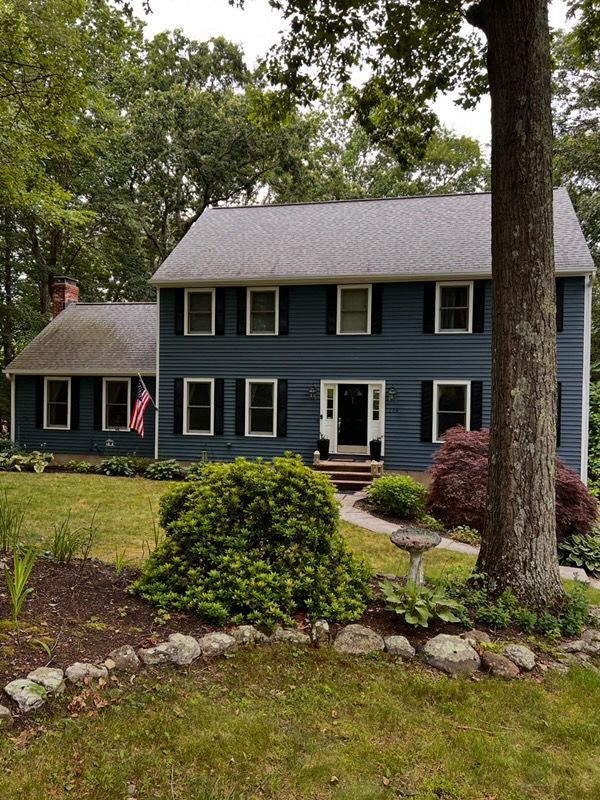 Two-story blue house with white trim and black shutters, set in a green lawn with trees.