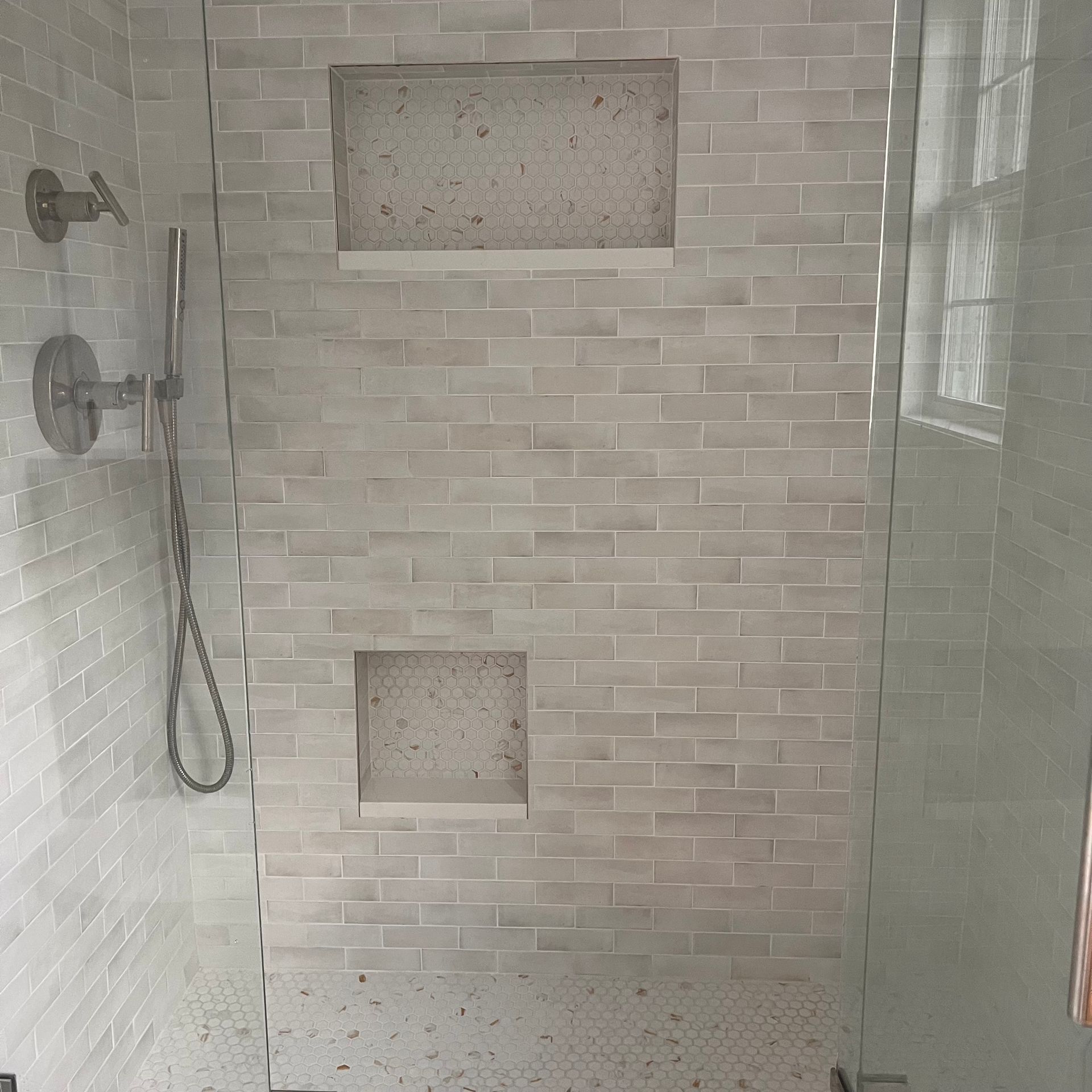 Shower with light gray brick-style tile and two built-in alcoves. A glass shower door and silver shower fixtures are visible.