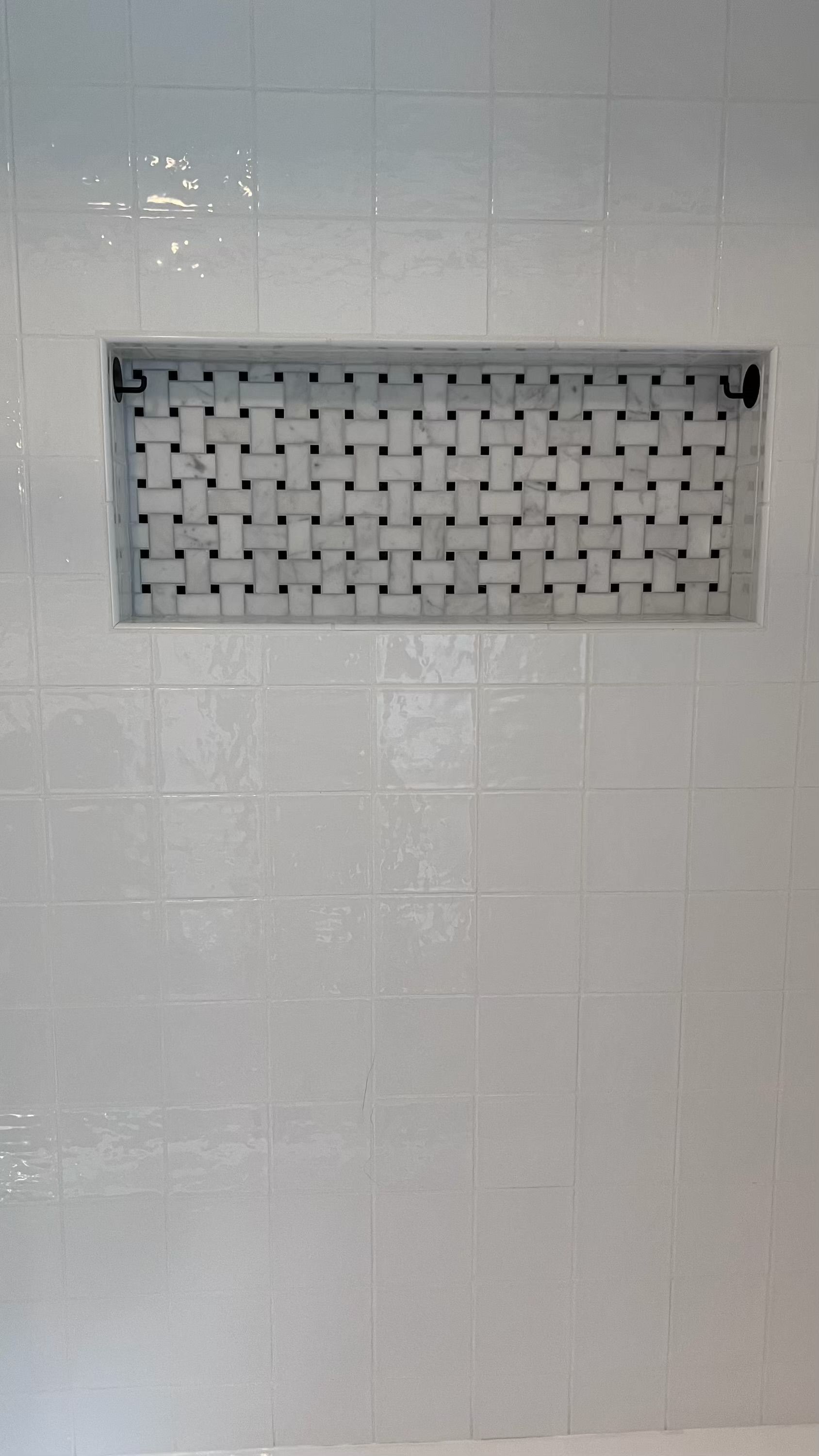 White tiled wall with a rectangular woven pattern inset, likely a shower design.