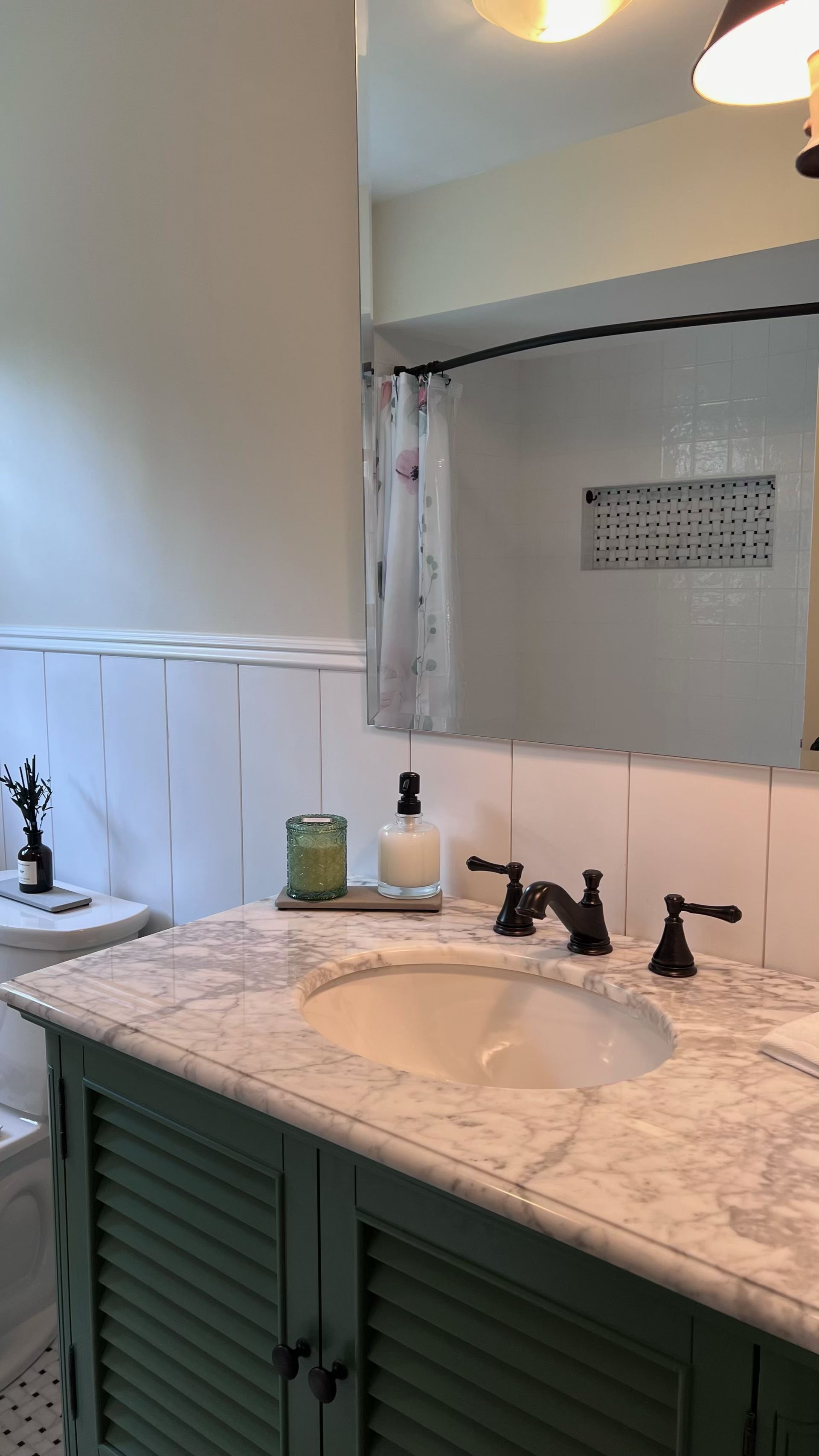 Bathroom with a green vanity, marble countertop, and black fixtures. A large mirror is above the sink.