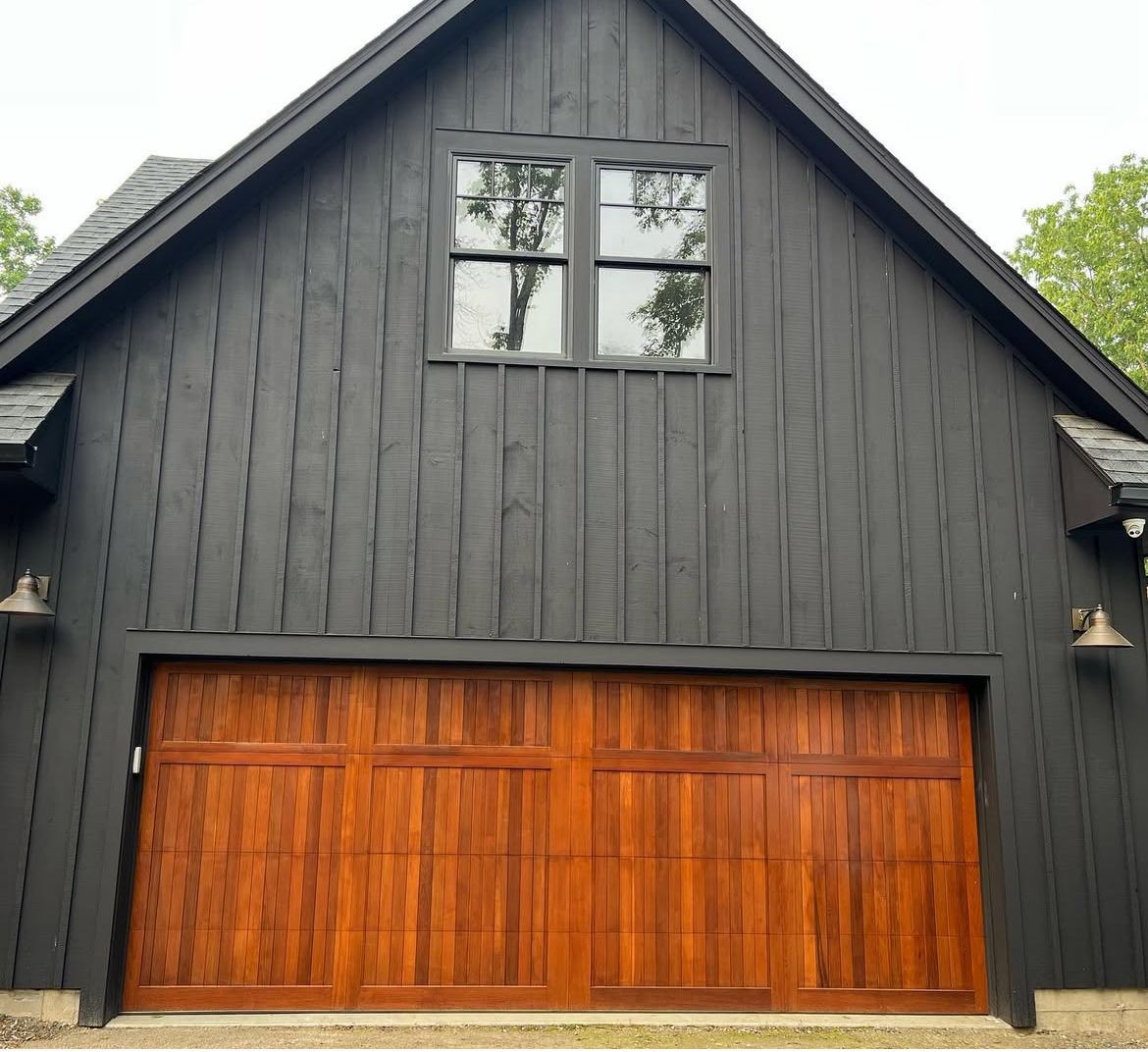 Black wooden building with a brown wooden garage door, small window, and two sconces.