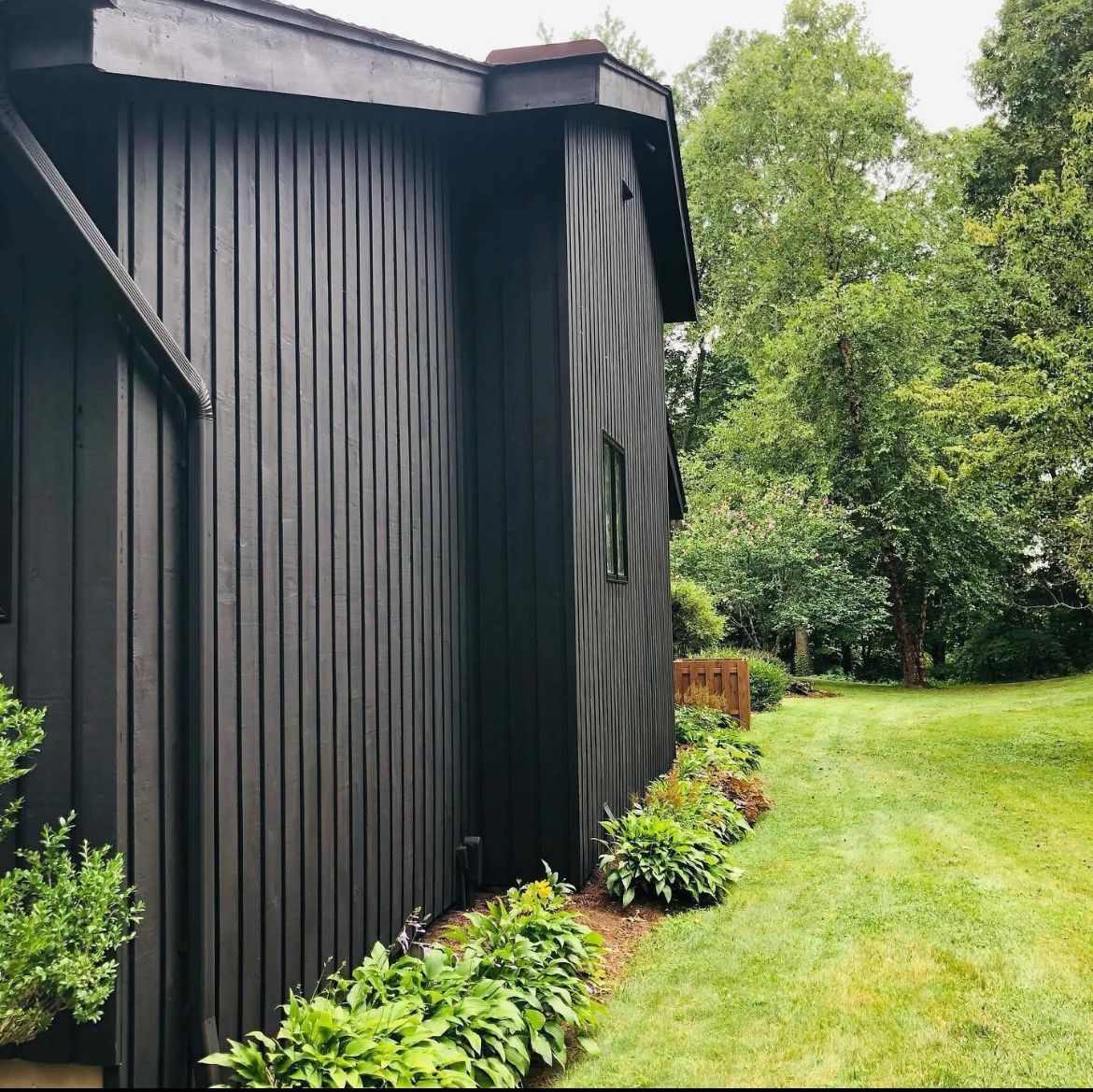 Black-painted house with vertical wood siding, bordered by greenery and a grassy yard.