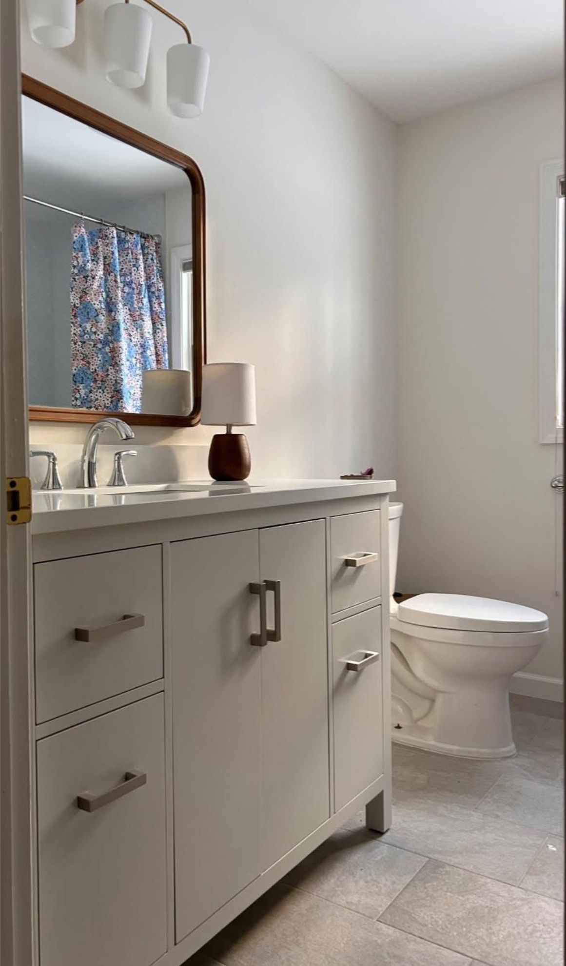 White bathroom with a vanity, toilet, and large mirror. A patterned shower curtain is visible.