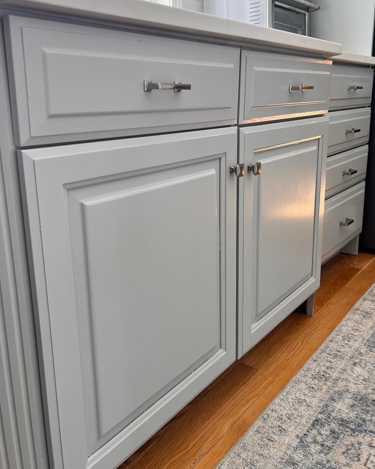 Light gray kitchen cabinets with silver hardware and a white countertop.