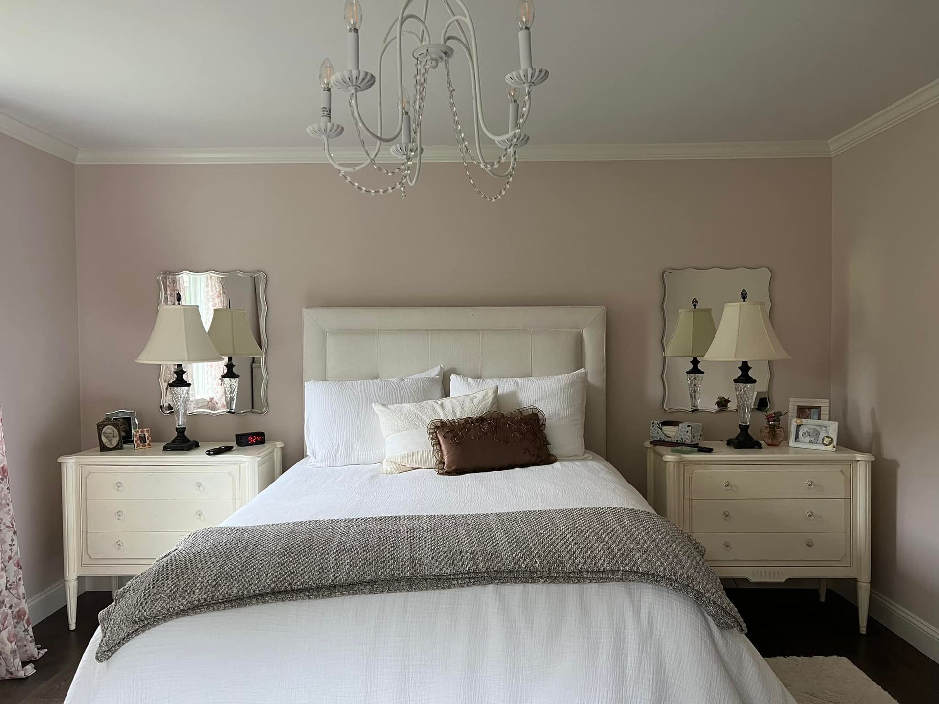 Bedroom with a bed, nightstands, lamps, mirrors, and chandelier. Walls are pink and trim is white.