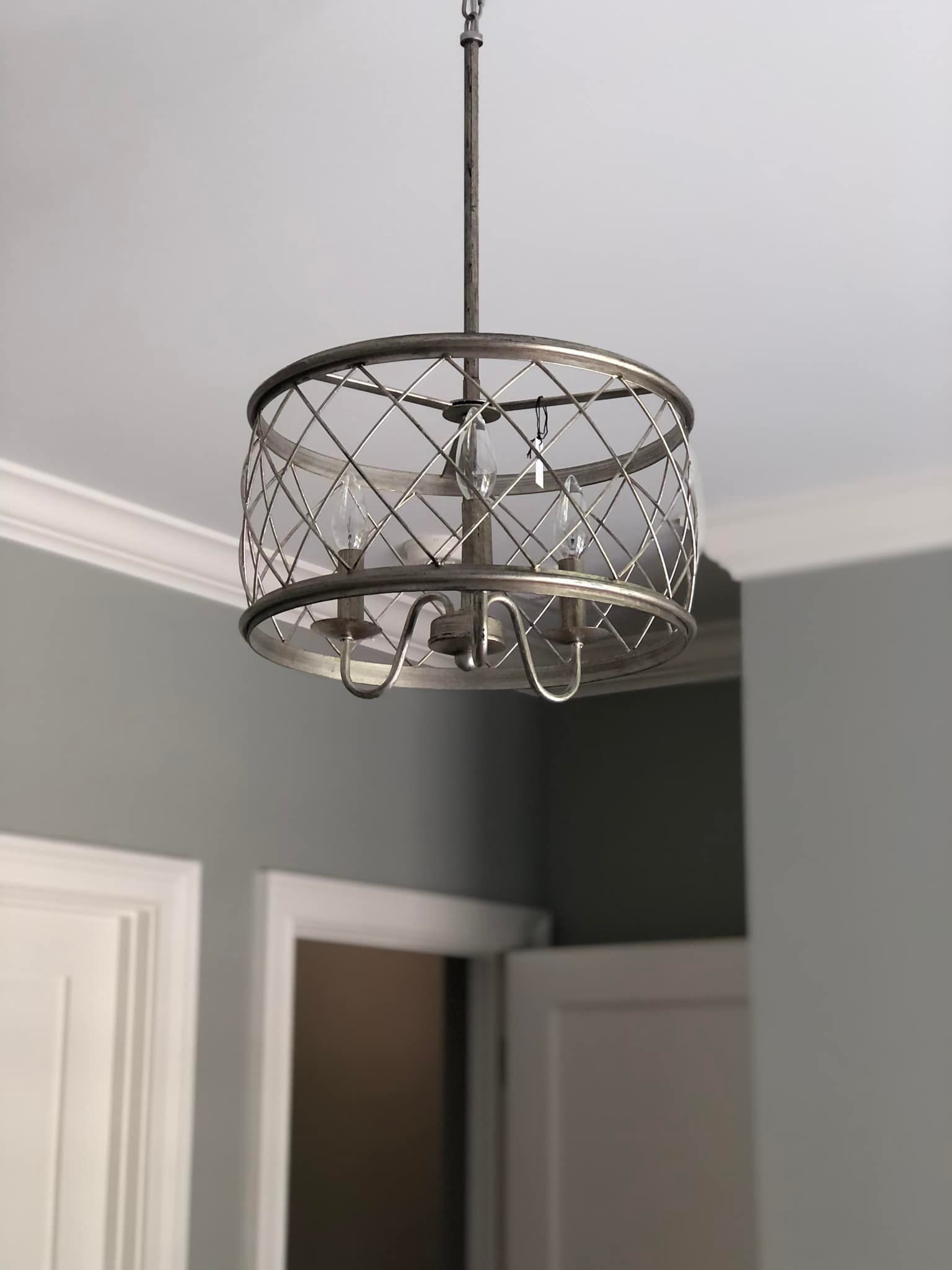 Silver chandelier hanging from a white ceiling, with a patterned cage-like design; walls are gray.