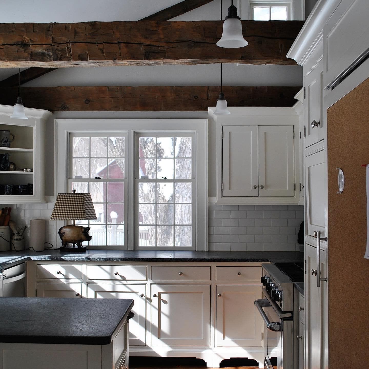 Cozy kitchen with white cabinets, dark countertops, and exposed wooden beams. Sunlight streams through windows.
