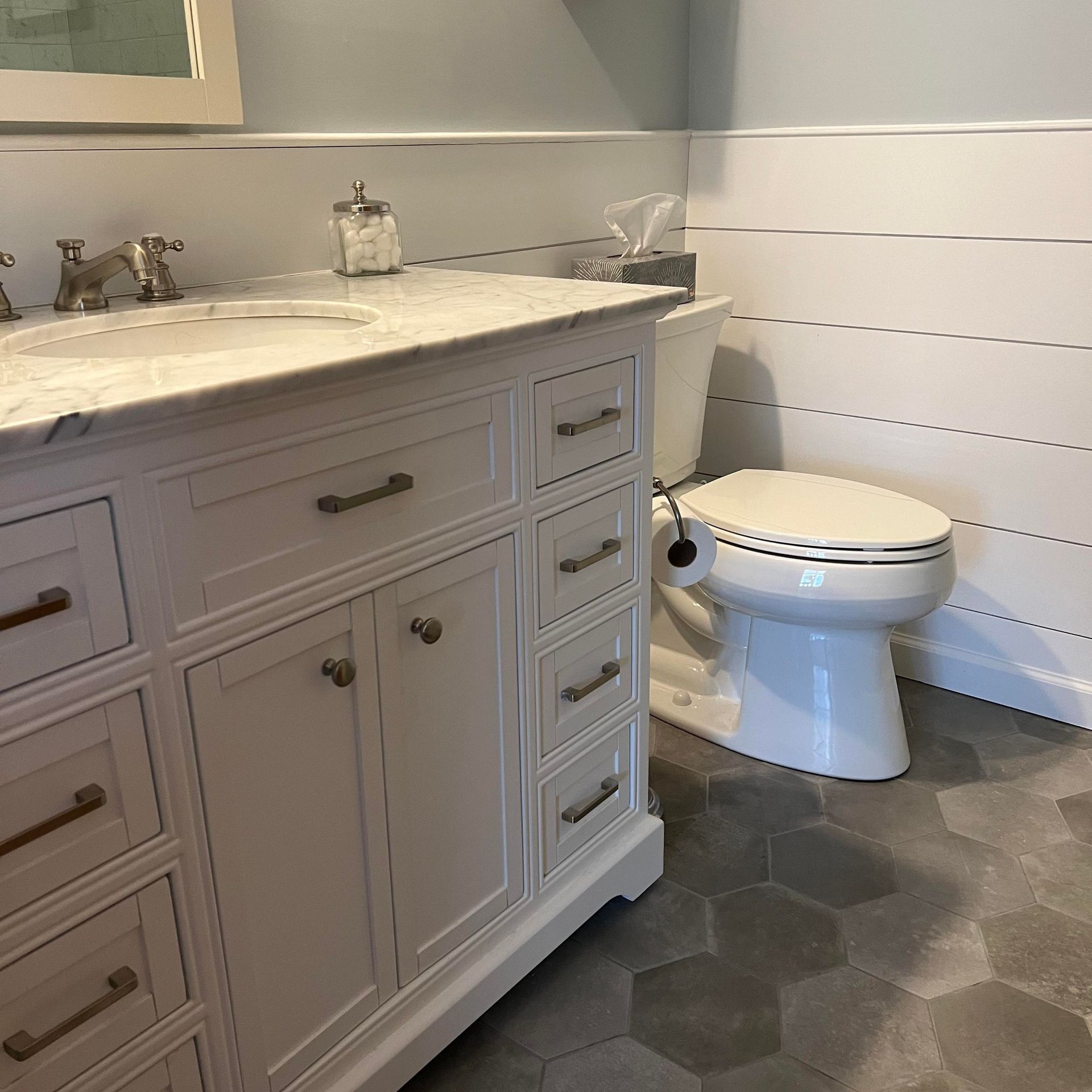 White bathroom with vanity, toilet, and hexagon tile floor.