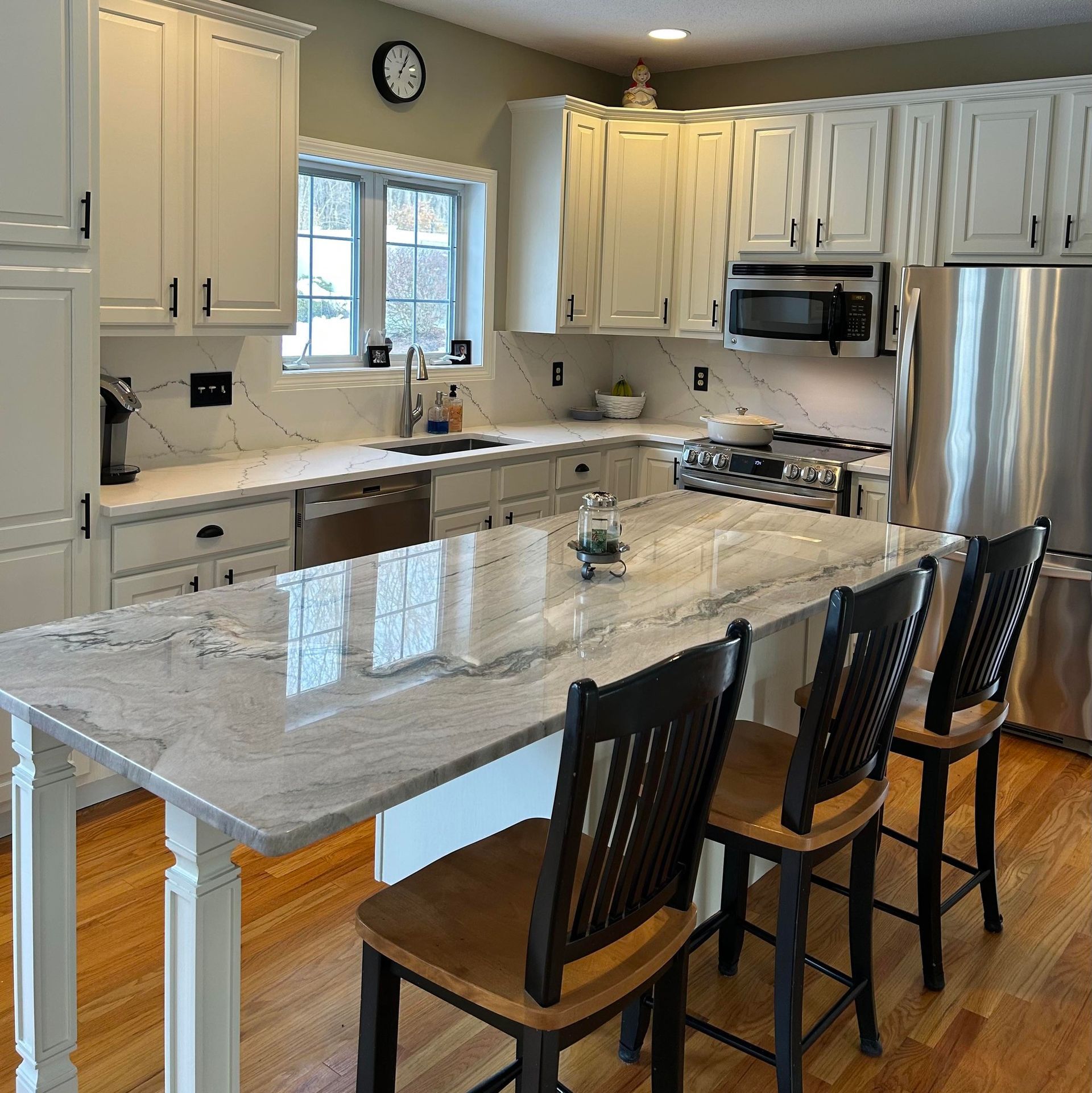 White kitchen with a marble countertop island and three stools. Stainless steel appliances and cabinets.