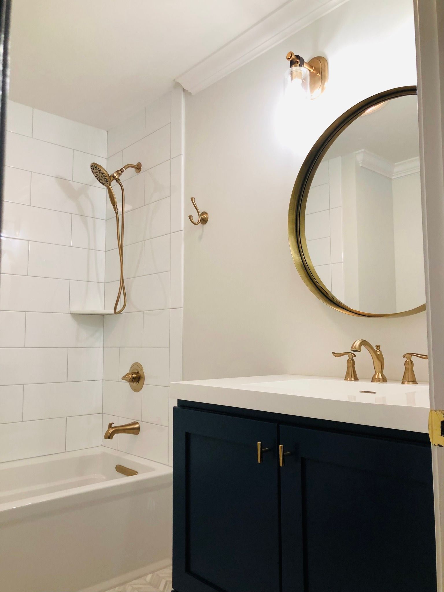 Bathroom with white tile, gold fixtures, navy vanity, and round gold mirror.